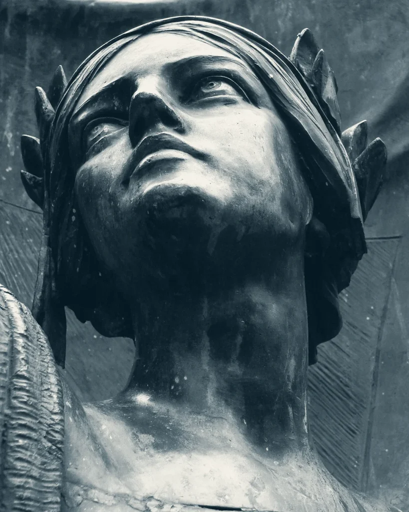 Black-and-white photograph of a bronze statue’s face, looking upward